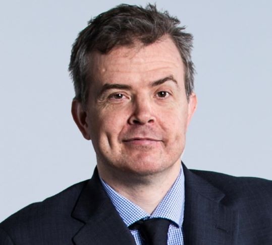 A man, Ben Gauntlett Disability Discrimination Commissioner looking at the camera wearing a black jacket, blue shirt and tie